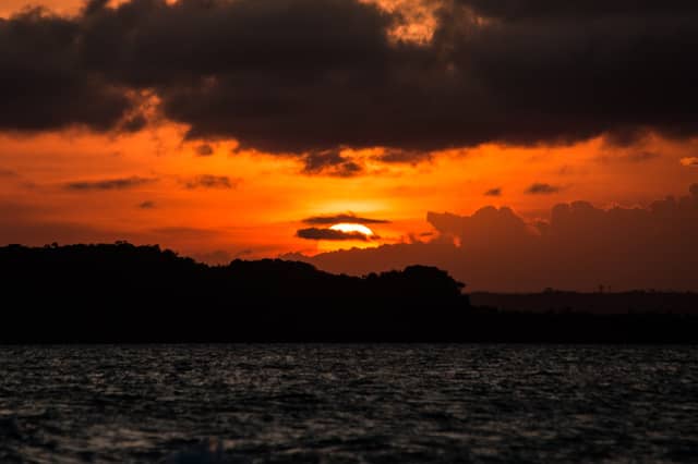 Pôr do sol em tons de laranja e vermelho intenso sobre a silhueta da Mata Atlântica na costa de Itacaré, refletido nas águas escuras e agitadas
