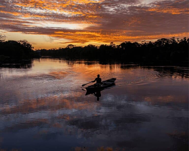 Pessoa remando uma canoa de madeira num rio calmo da floresta ao pôr do sol, um momento clássico de um passeio na Amazônia saindo de Manaus