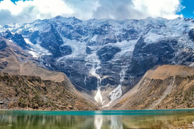 Glacier meltwater streaming down a snowy Andean wall into the turquoise water of Humantay Lake near the Salkantay trek