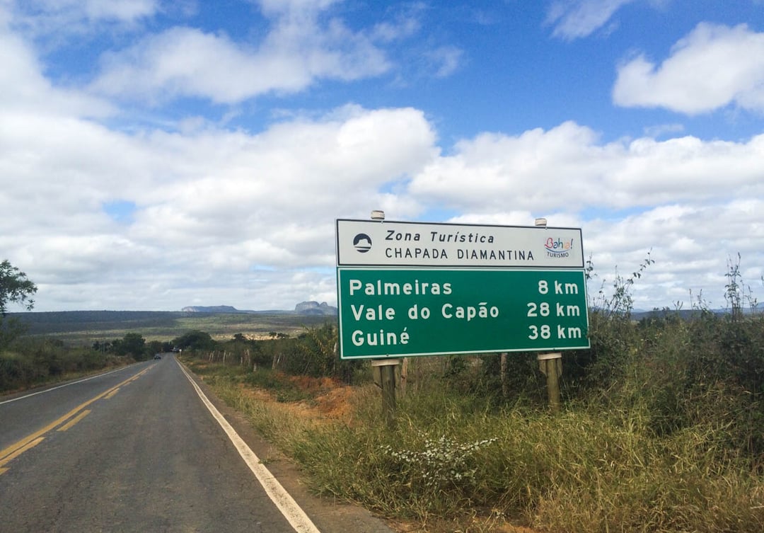 Ein grünes Straßenschild für die Touristenzone Chapada Diamantina, das die Entfernungen nach Palmeiras, Vale do Capão und Guiné anzeigt.