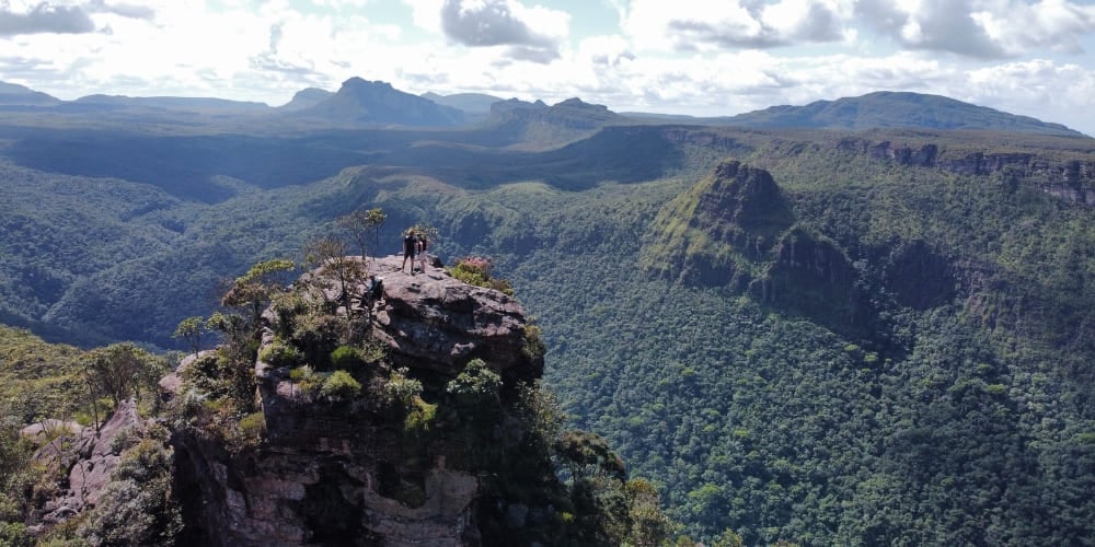 Wanderer stehen auf einem felsigen Gipfel am Morro do Castelo und blicken über einen riesigen, bewaldeten Canyon in der Chapada Diamantina.