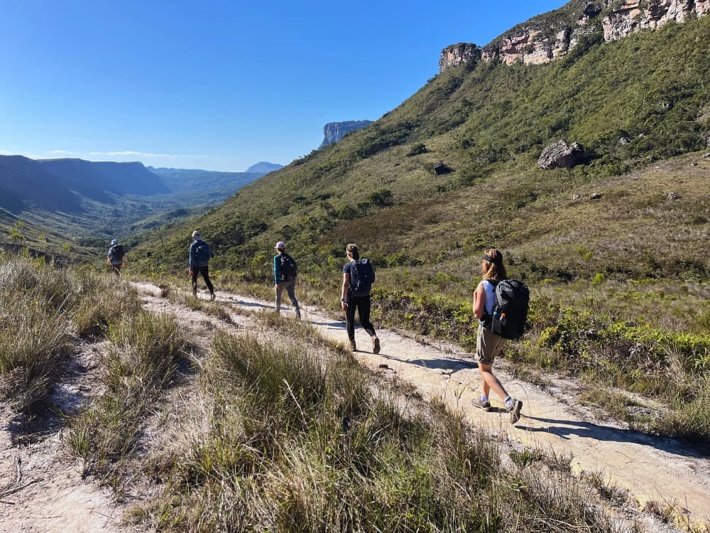 Um grupo de trilheiros caminha por uma trilha de terra cercada por montanhas verdes durante a estação seca no Parque Nacional da Chapada Diamantina.