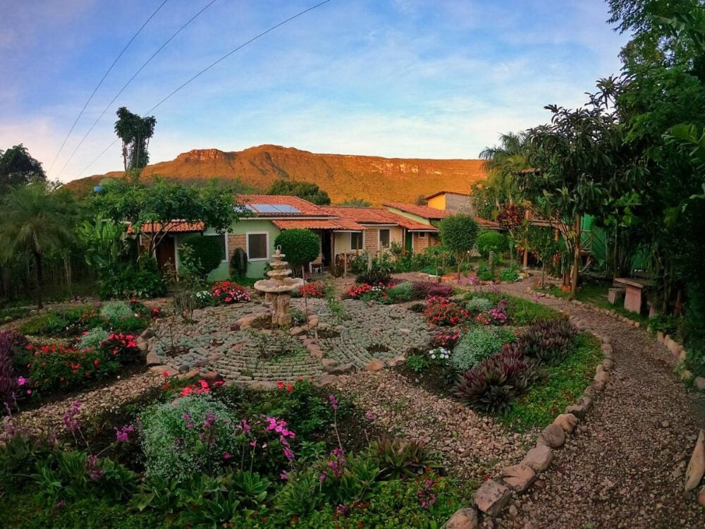 Um jardim circular bem cuidado com uma fonte de pedra em um retiro tranquilo, emoldurado por montanhas verdes na Chapada Diamantina.
