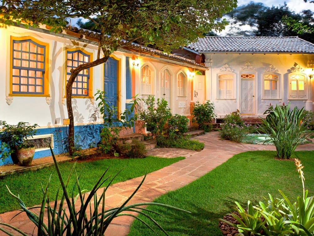Pátio em estilo colonial da Pousada Vila Serrano em Lençóis, com paredes azuis e brancas e jardins verdes exuberantes.