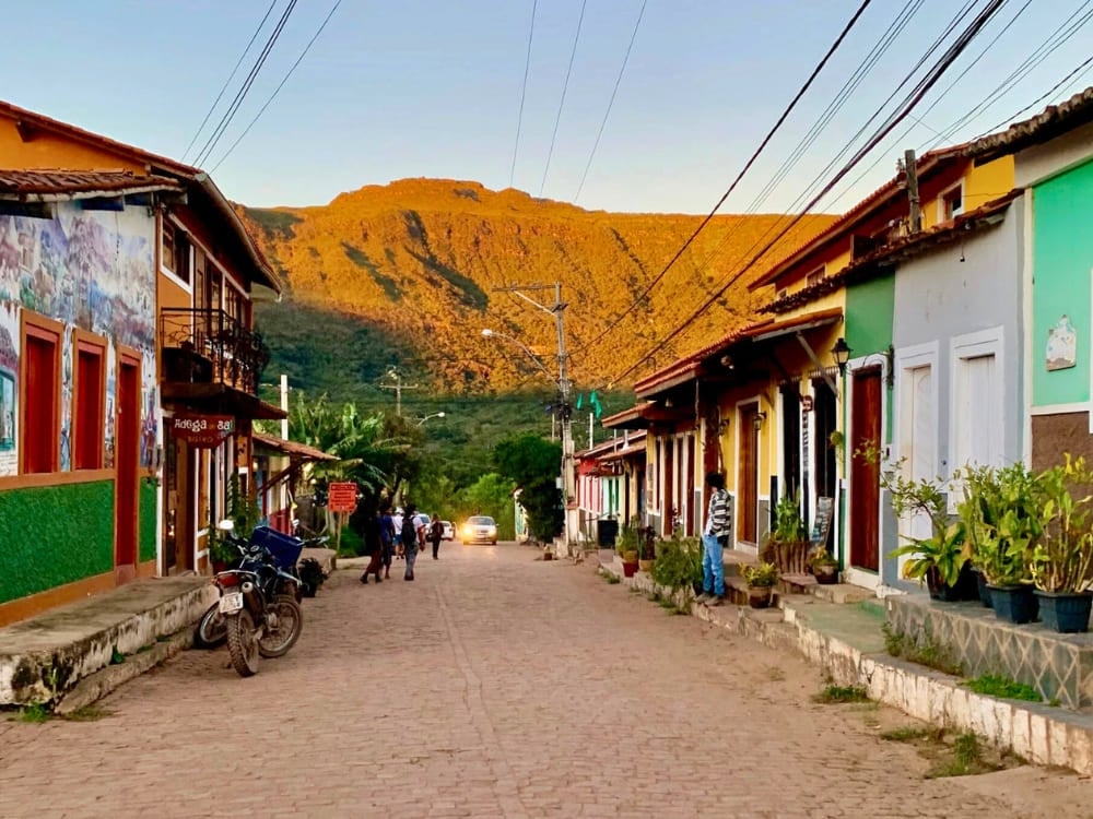 Casas coloridas alinhadas na pacata rua principal do Vale do Capão com uma enorme montanha brilhando ao pôr do sol.