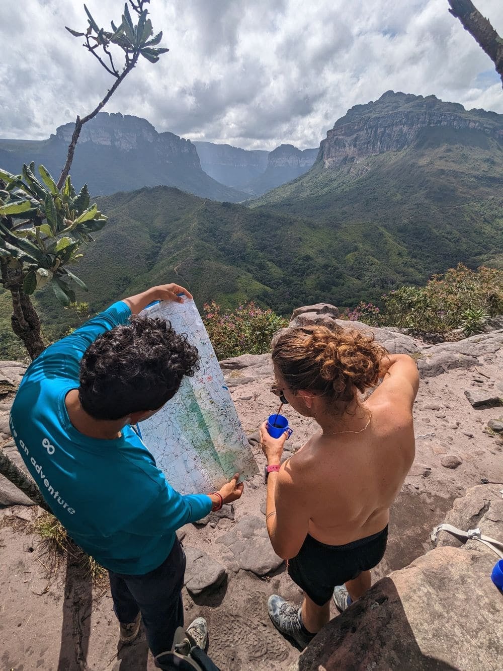 Um guia local e um viajante examinando um mapa juntos em um mirante alto com vista para um vale verde.