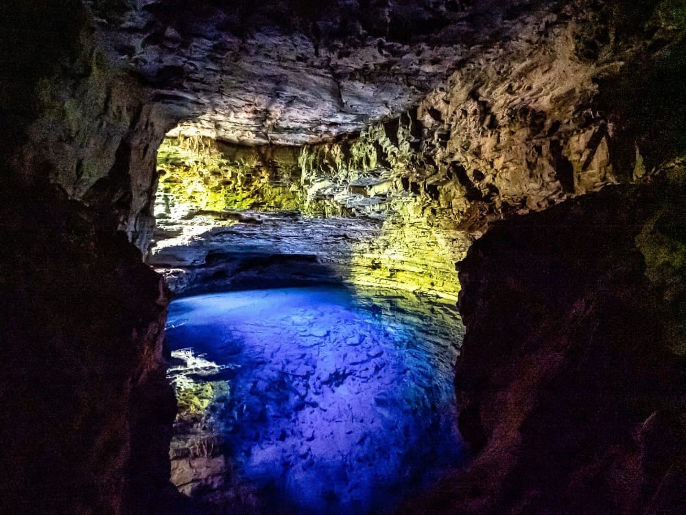 A luz do sol criando efeitos surreais na superfície azulada da água dentro de uma caverna no Poço Azul.