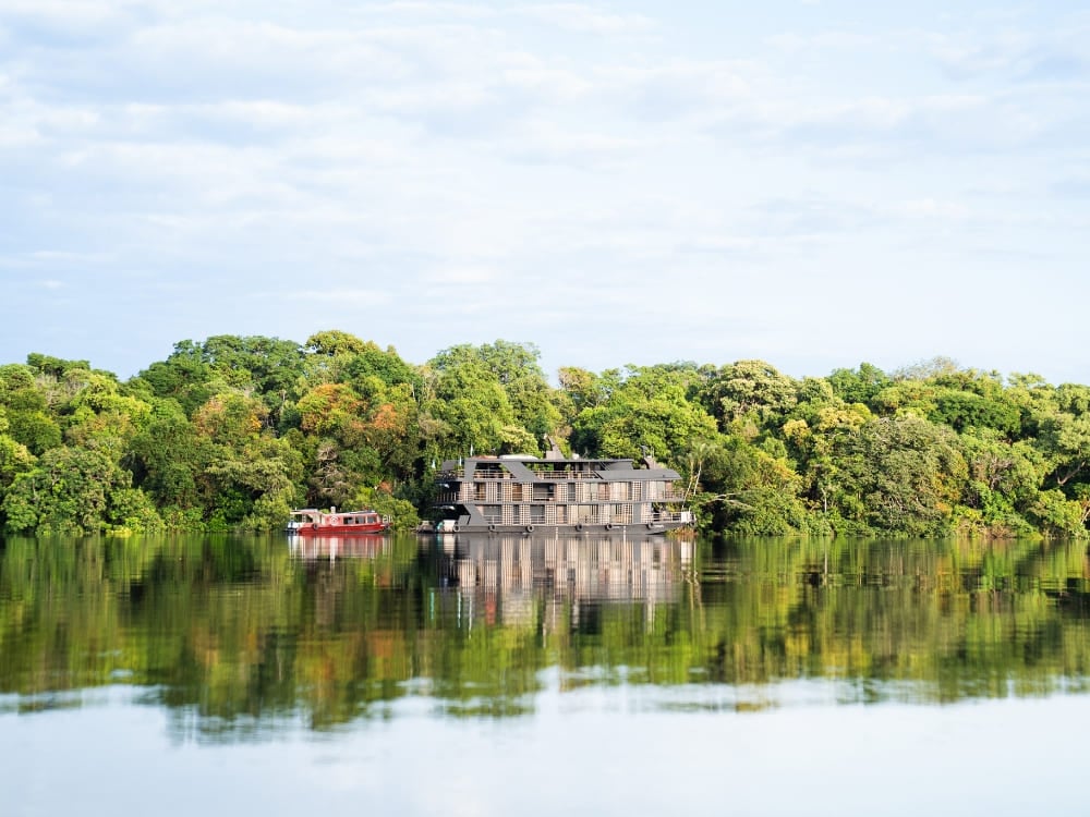 Un bateau à plusieurs ponts pour une croisière de luxe en Amazonie, flottant sur des eaux calmes reflétant la végétation dense de la forêt.