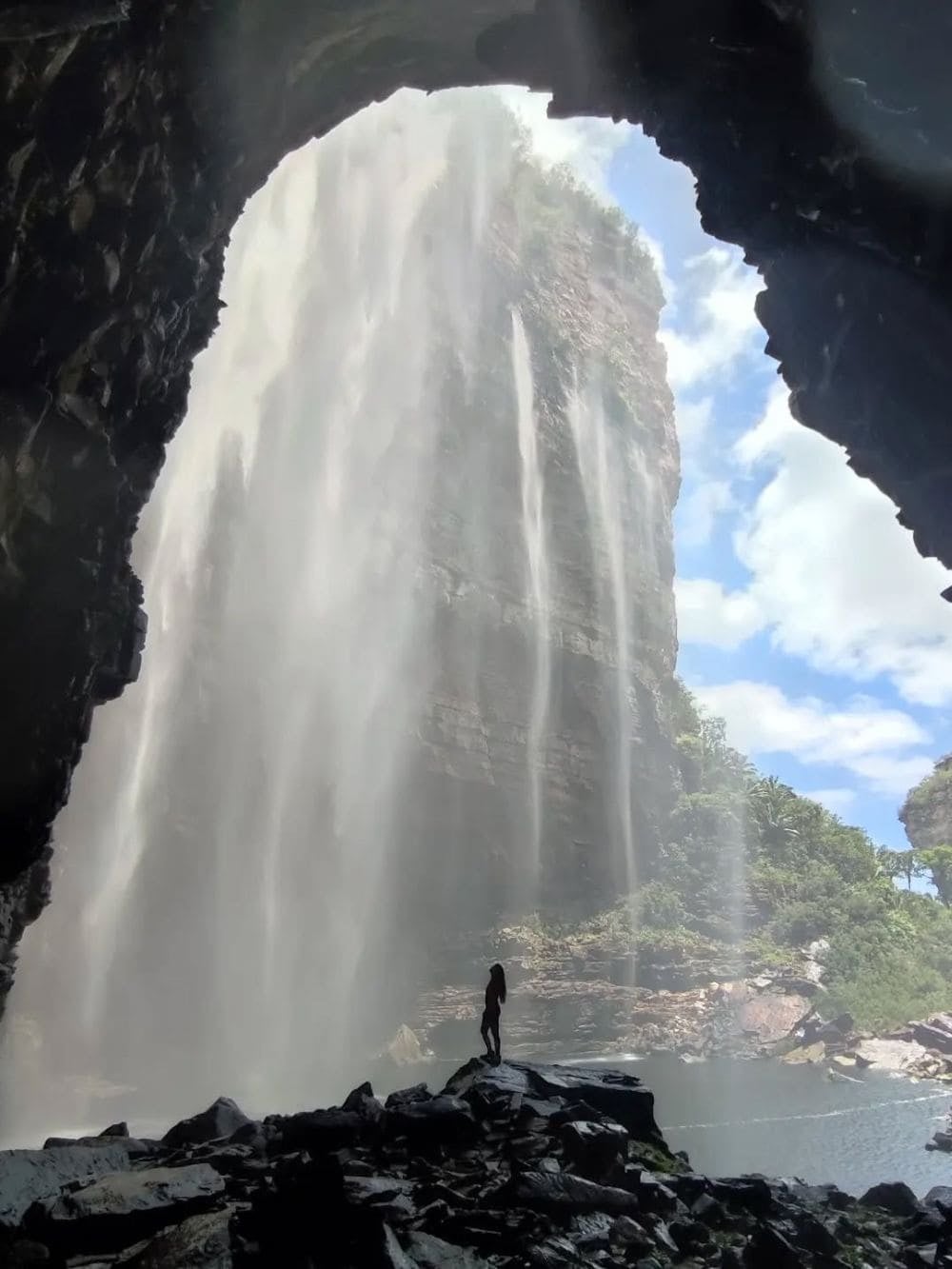 Silhueta de um trilheiro de pé sobre rochas na base da enorme cachoeira do Buracão, fluindo dentro de um cânion.