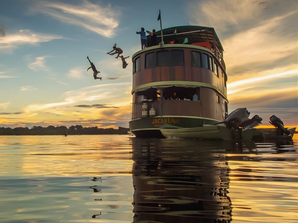 Des voyageurs sautant du pont supérieur d'un bateau de croisière de luxe sur l’Amazone au coucher du soleil.
