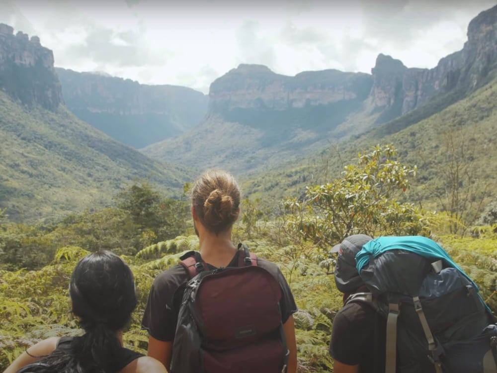 Três viajantes com mochilas observando um vasto vale verde no coração da Chapada Diamantina.