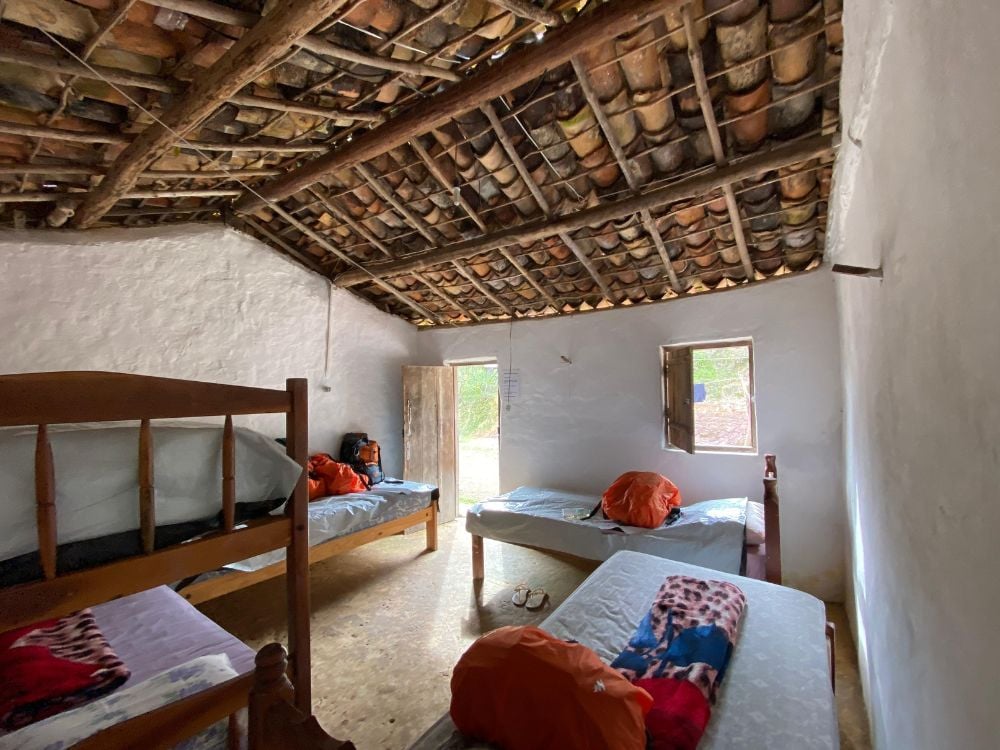 Um quarto de hóspedes compartilhado com camas de madeira e sacos de dormir sob um teto rústico com telhas e madeira aparentes.