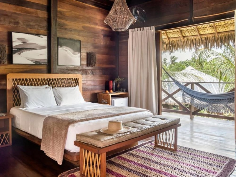 Gemütliches, mit dunklen Holzpaneelen verkleidetes Zimmer im Charme Atins, ausgestattet mit einem Doppelbett und offenen Türen zu einem Balkon mit Hängematte.