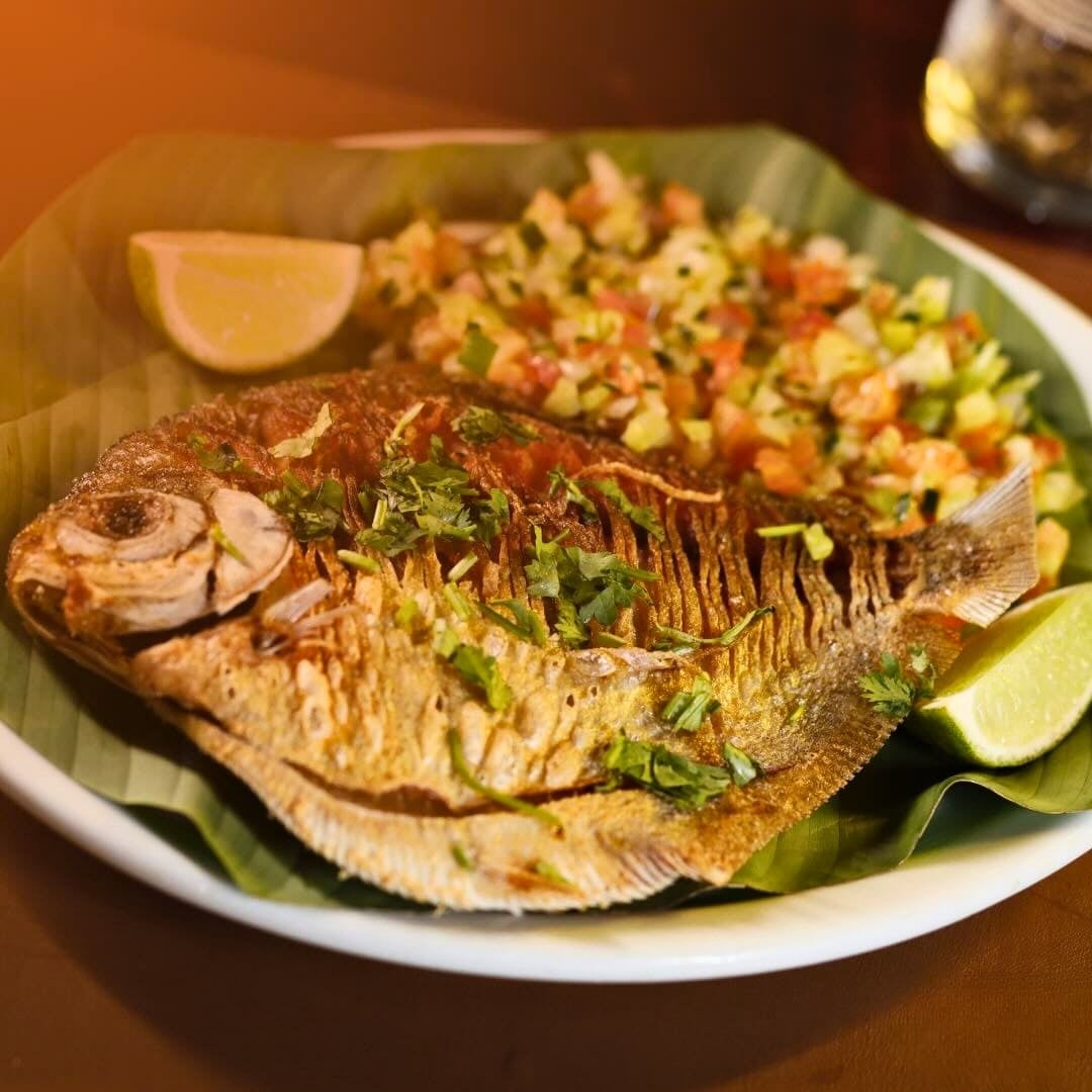  Grilled Tambaqui fish served whole on a banana leaf with vinaigrette and lime slices.