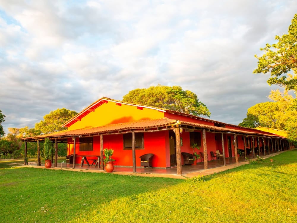 L'extérieur rouge de l'auberge SouthWild Pantanal présente un porche en bois ombragé pour les voyageurs en quête d'un séjour authentique.