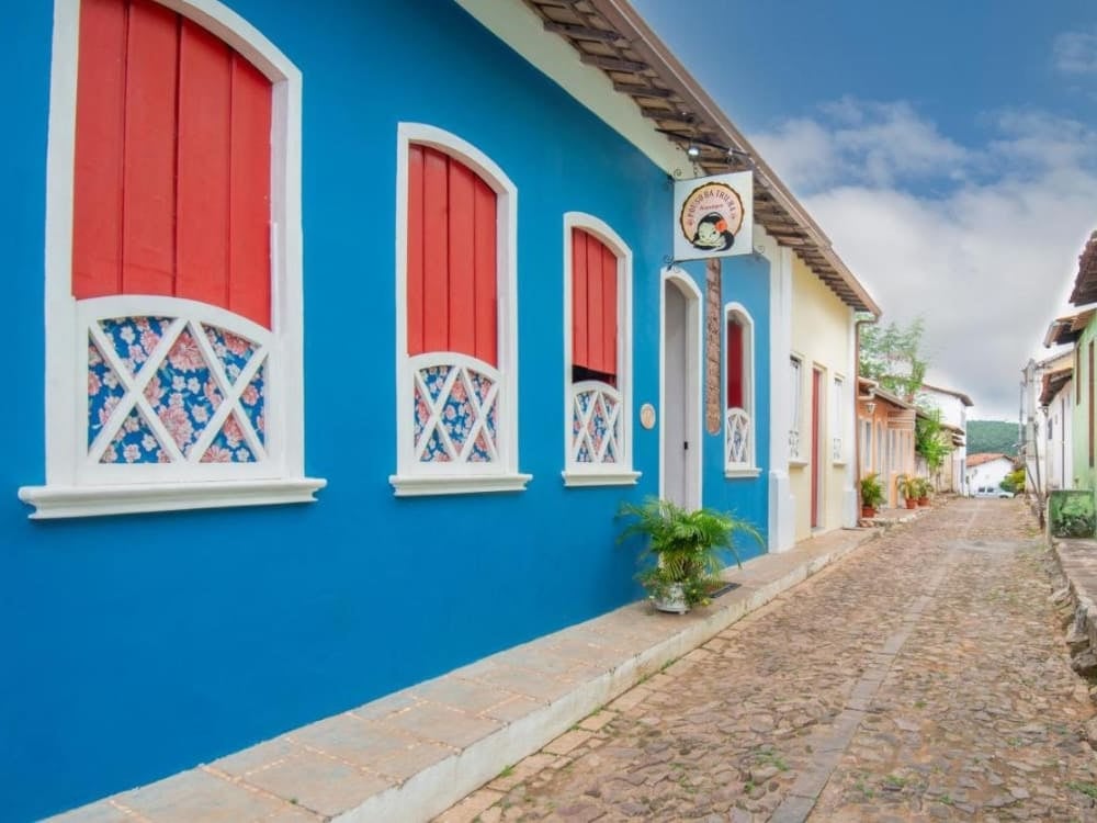 Bright blue facade with white and red window frames of Pousada Alto do Cajueiro on a cobblestone street in Lençóis. 