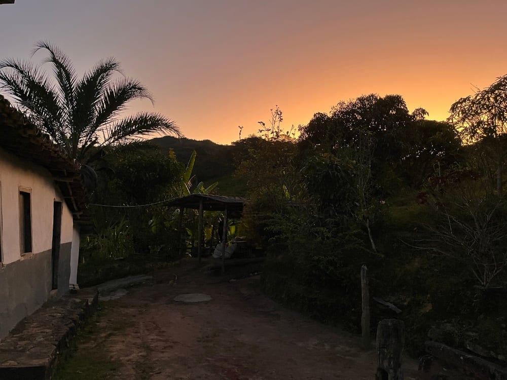 Silhouette of a local homestay and palm trees in Vale do Pati against a vibrant orange sunset.