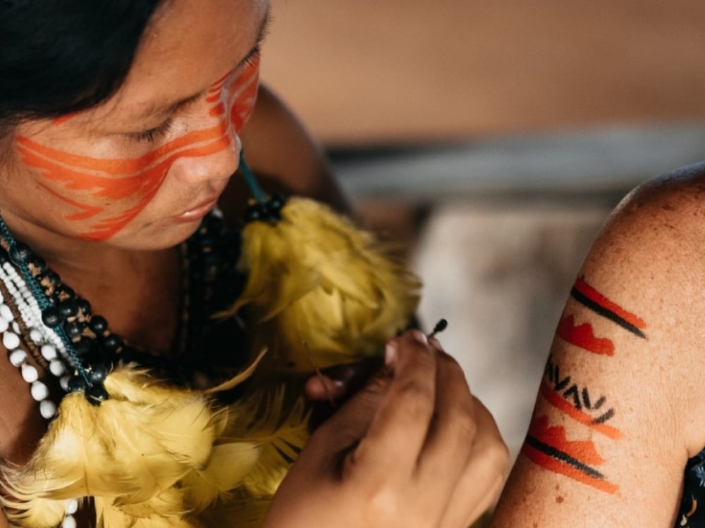 Femme indigène appliquant une peinture faciale traditionnelle rouge et noire, représentant la riche culture des communautés locales en Amazonie, soutenues par l'écotourisme.