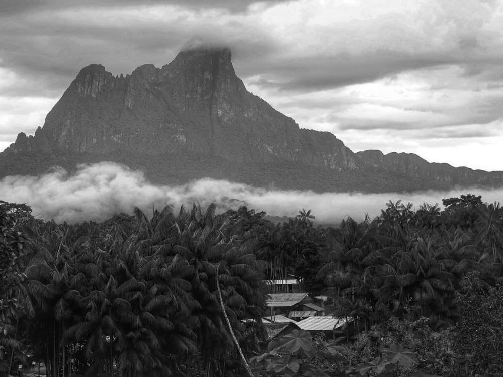 O pico maciço do Pico da Neblina elevando-se acima de uma extensão verde infinita de árvores amazônicas sob um céu azul.