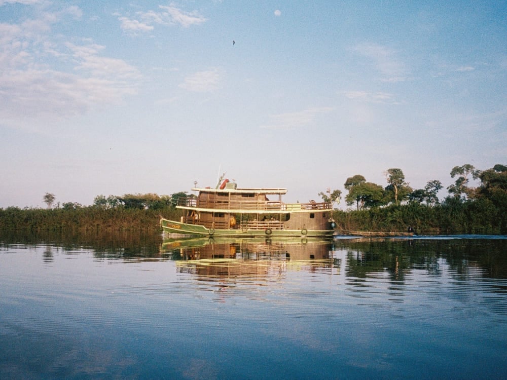 Traditional river cruise boat navigating the calm waters of the Rio Negro, with green vegetation reflecting on the water.