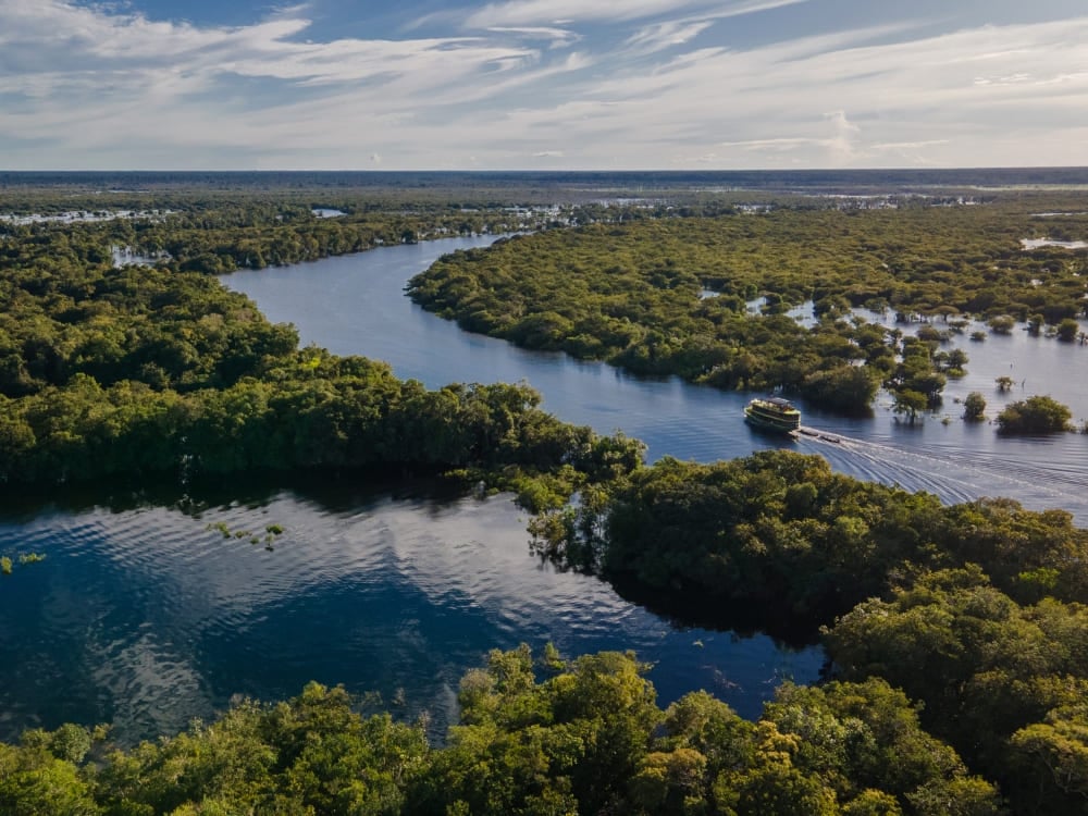 Um barco fluvial navegando pelas águas sinuosas do Rio Amazonas cercado pela exuberante floresta tropical.