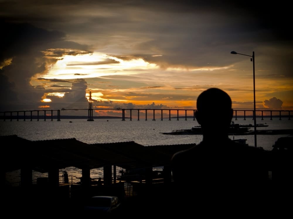 Silhueta de um viajante observando o pôr do sol sobre o Rio Amazonas em Manaus, a porta de entrada para a floresta.