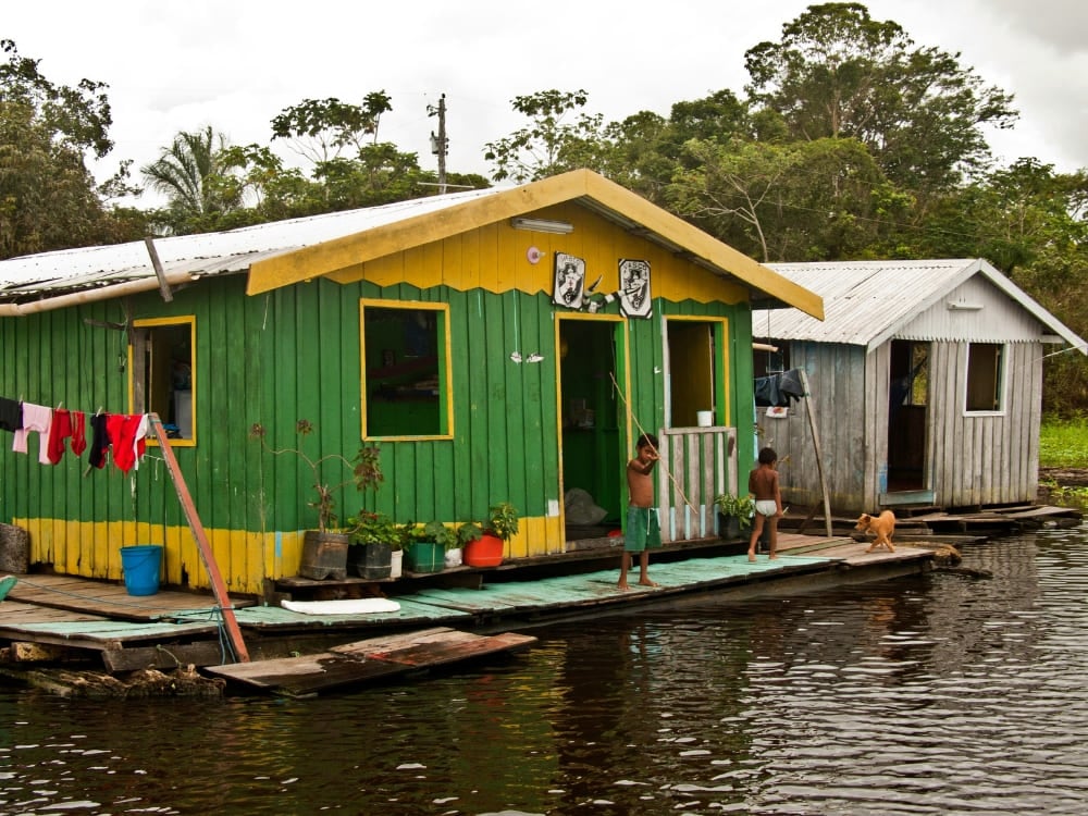 Crianças em frente a uma vibrante casa flutuante verde e amarela nas águas do Rio Amazonas.