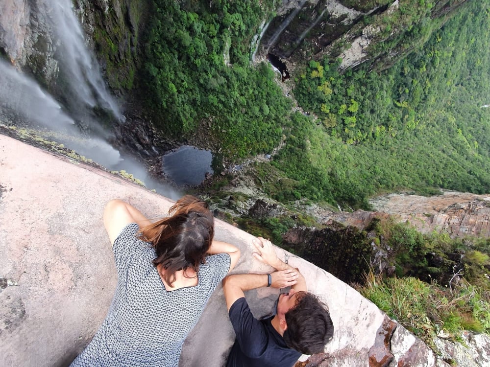 Twee wandelaars kijken vanaf een hoge klifrand naar beneden naar de Cachoeirão-waterval die zich in de diepgroene Vale do Pati-kloof stort.