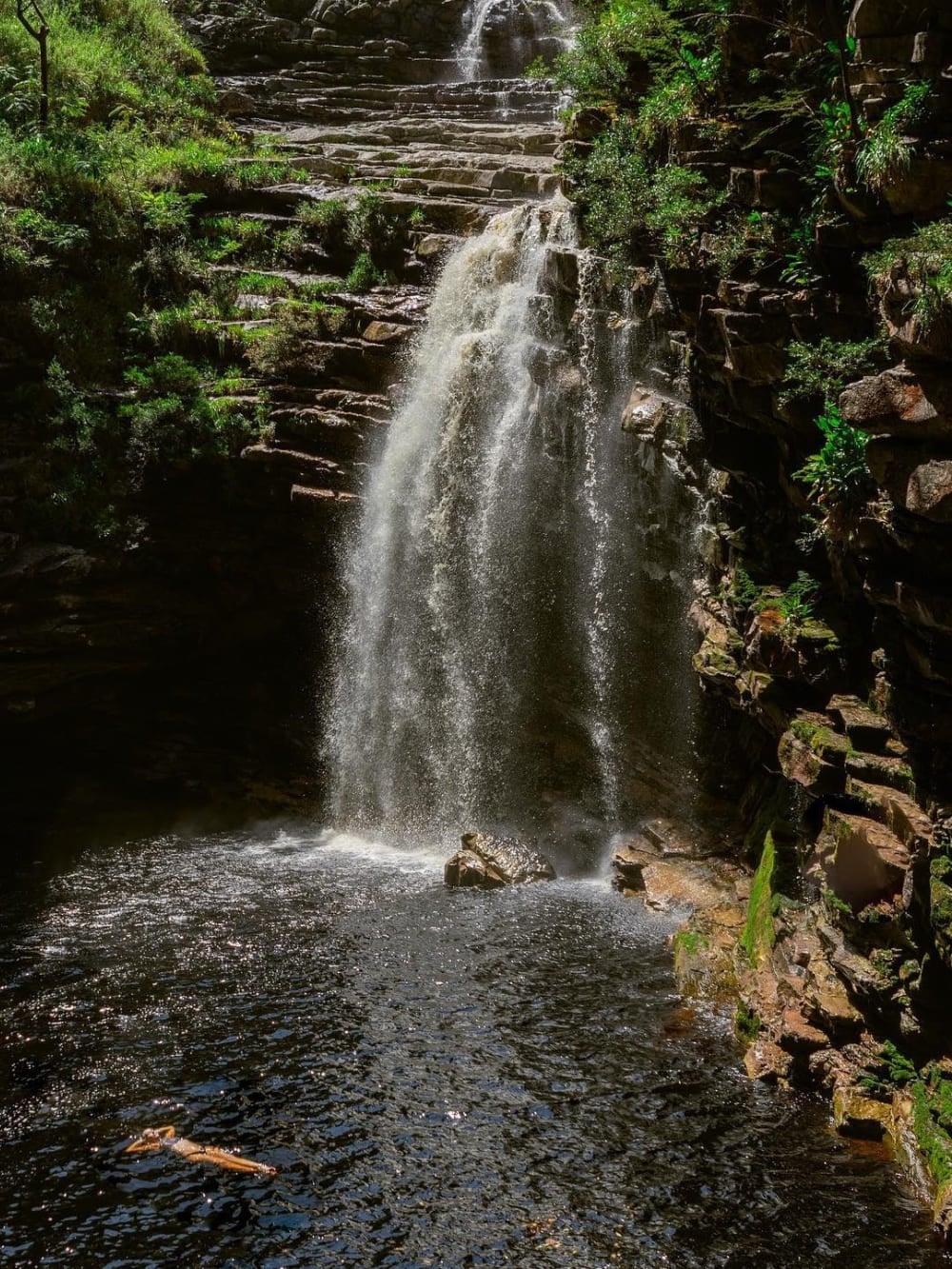 Een persoon zwemt in het vredige, donkere natuurlijke zwembad aan de basis van de 20 meter hoge Sossego-waterval in de buurt van Lençóis.