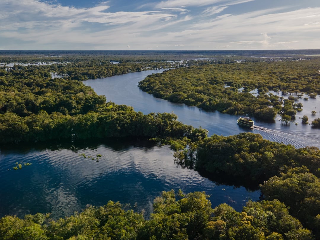 Luchtfoto van een rivierboot die zich een weg baant door het overstroomde bos en de riviergeulen van het Braziliaanse Amazonegebied.