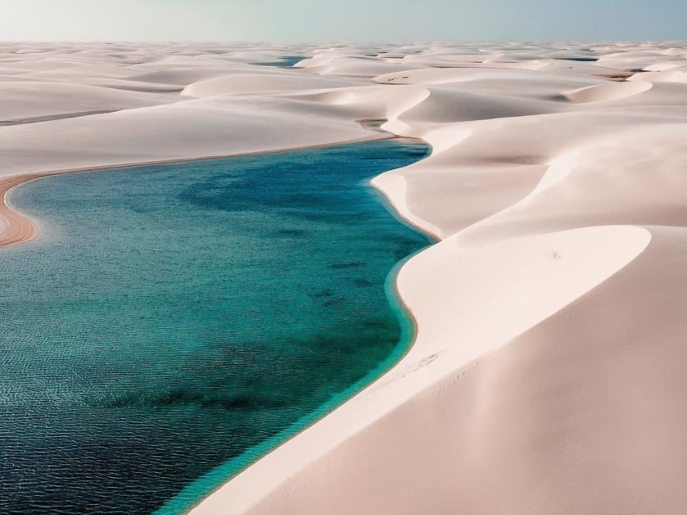 Luftaufnahme einer langen türkisfarbenen Lagune, die sich zwischen den weißen Sanddünen der Lençóis Maranhenses windet.