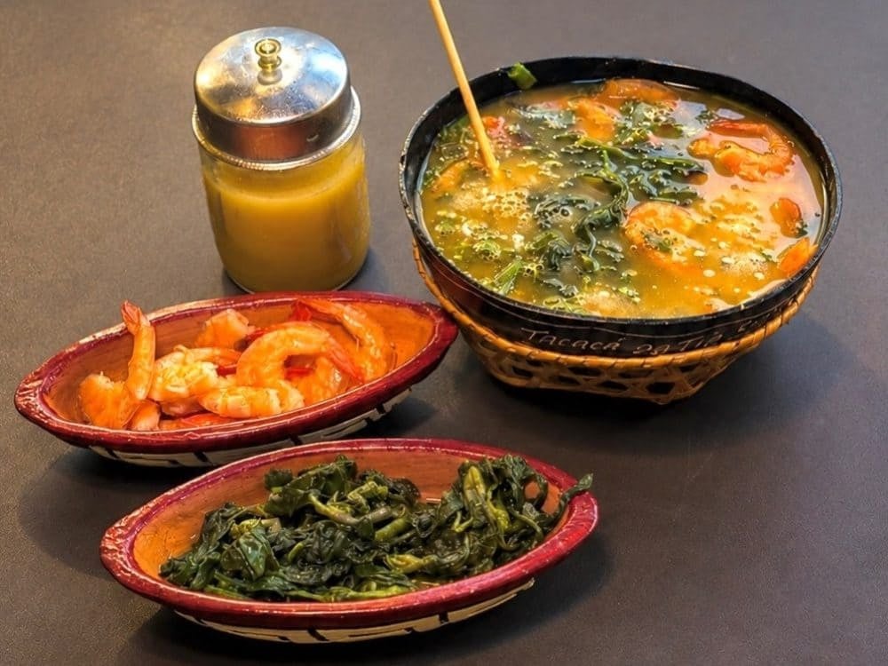 A cuia of tacacá with jambu and dried shrimp, beside bowls of shrimp, jambu and a jar of tucupi