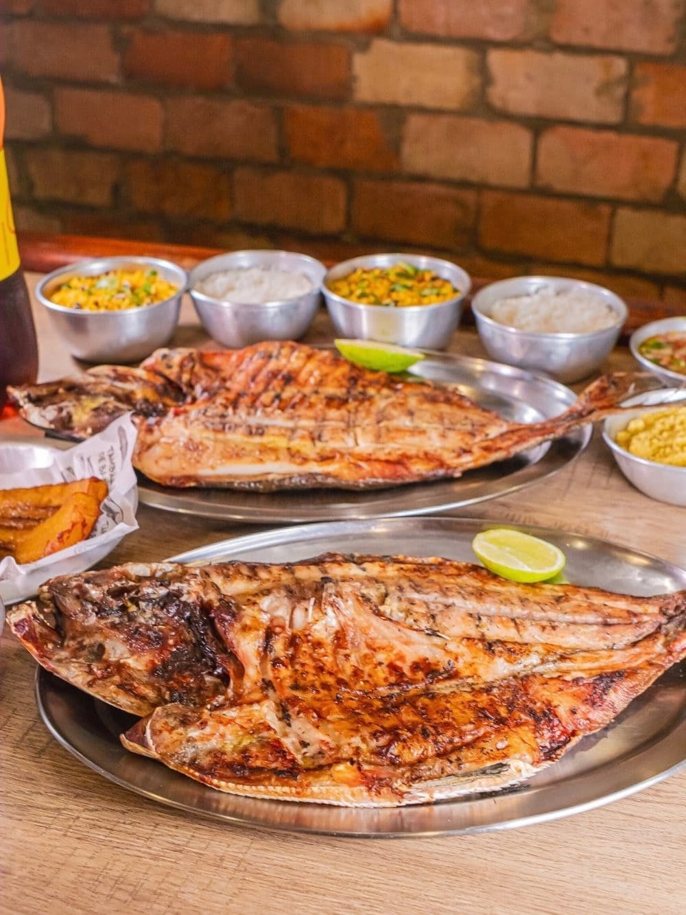 Two whole tambaqui grilled and split open on metal platters, served with lime, rice and farofa