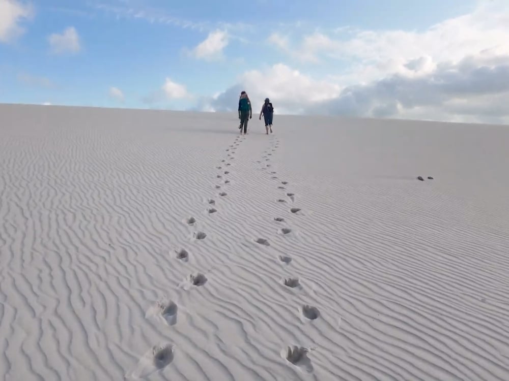Zwei Trekker überqueren eine geriffelte weiße Düne in den Lençóis Maranhenses und hinterlassen eine Spur aus Fußabdrücken