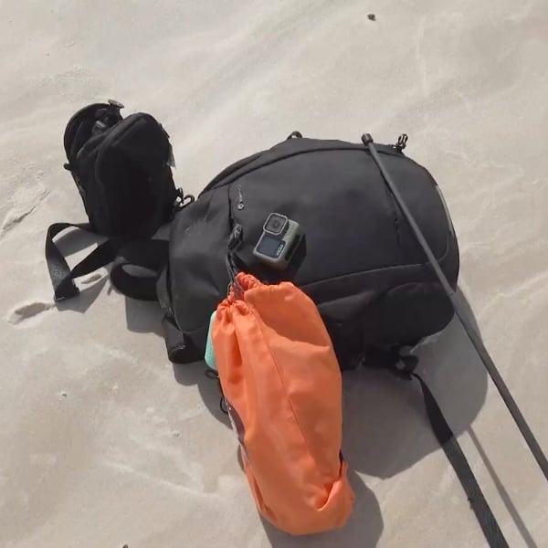 Rucksäcke, eine Actionkamera und ein oranger Packsack liegen während einer Pause beim Trekking im Sand