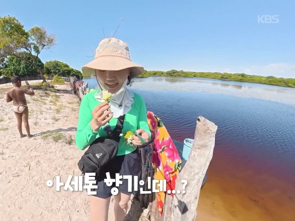 Jihee Yeon tiene in mano dei piccoli fiori gialli in riva all’acqua, con un bambino del posto sullo sfondo