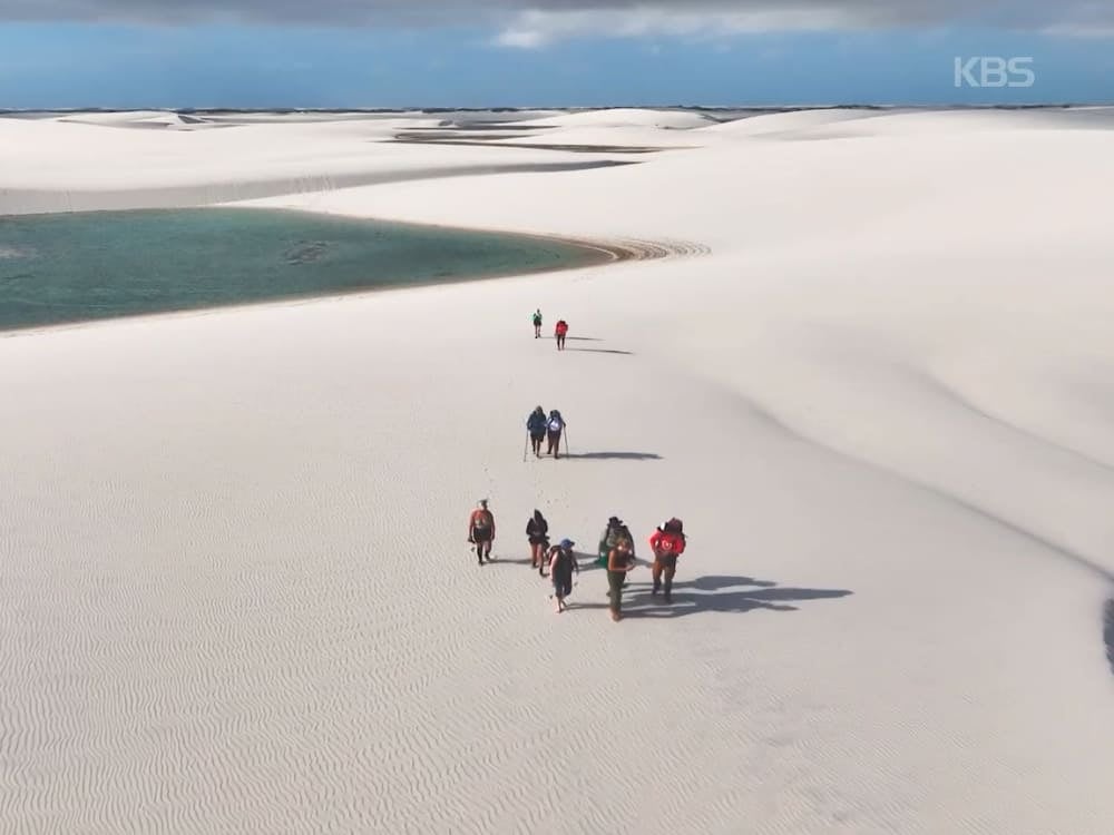Un gruppo di escursionisti attraversa le dune bianche accanto a una laguna nel Parco Nazionale dei Lençóis Maranhenses