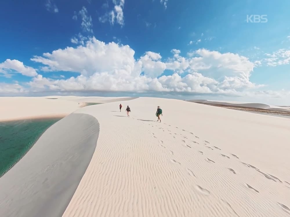 Escursionisti camminano su una duna di sabbia bianca accanto a una laguna turchese nei Lençóis Maranhenses
