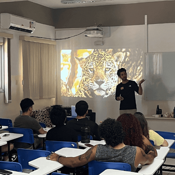 Onçafari staff member giving a talk to a full classroom with a jaguar photo projected on the wall