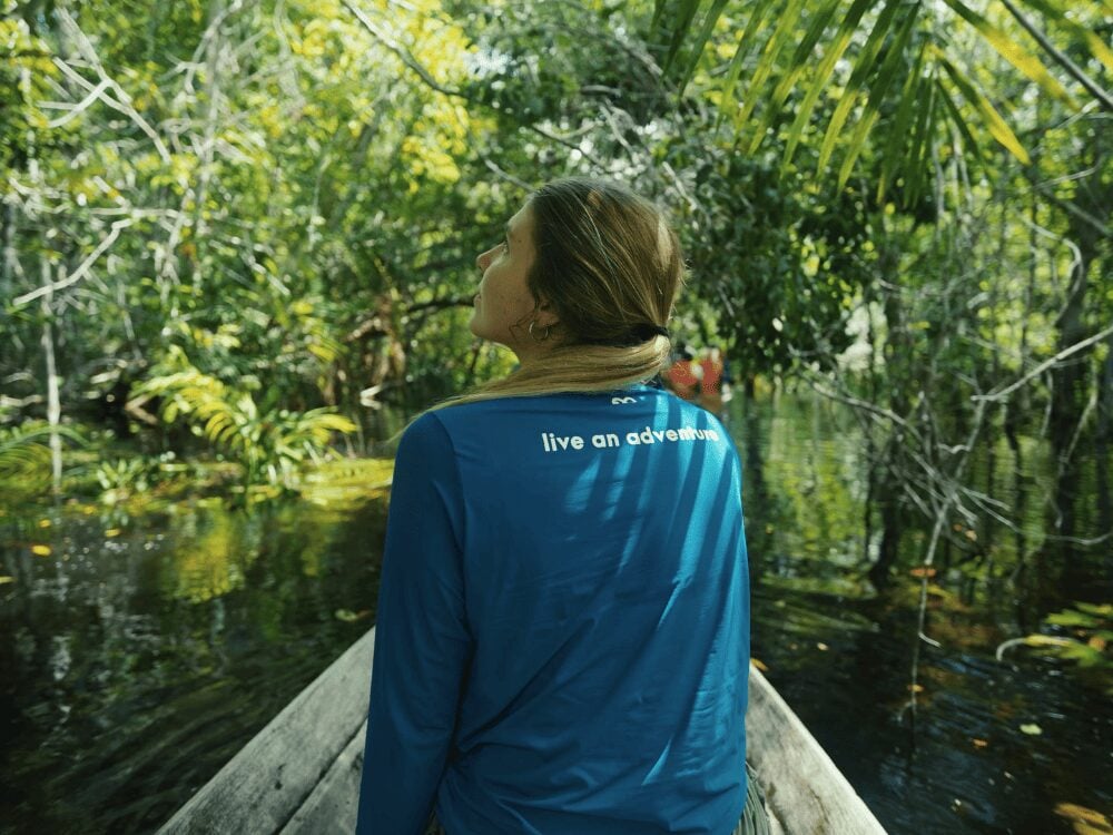 Viajante de costas numa canoa de madeira navegando por um canal de floresta alagada durante um passeio de vários dias na Amazônia saindo de Manaus