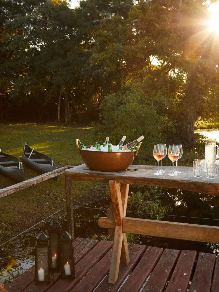Sunset drinks table on a wooden deck by the water at Caiman, with canoes resting on the bank
