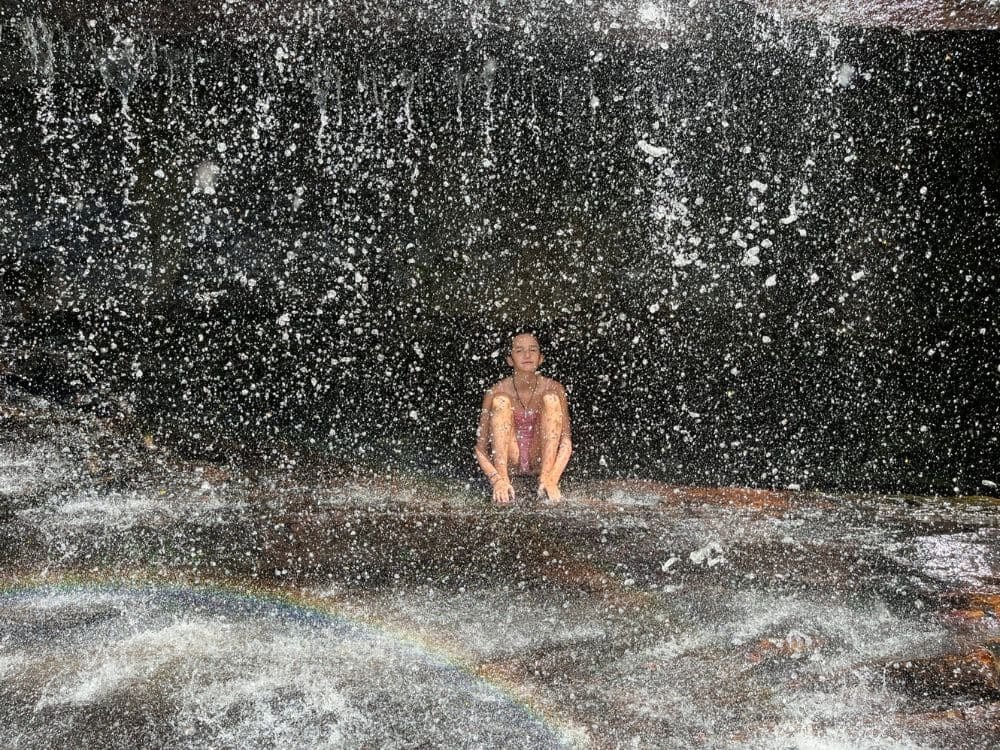 Turista relaxando sentado diretamente sob o grande fluxo de água refrescante de uma cachoeira no Parque Nacional da Chapada Diamantina. Turista relaxando sentado diretamente sob o grande fluxo de água refrescante de uma cachoeira no Parque Nacional da Chapada Diamantina.