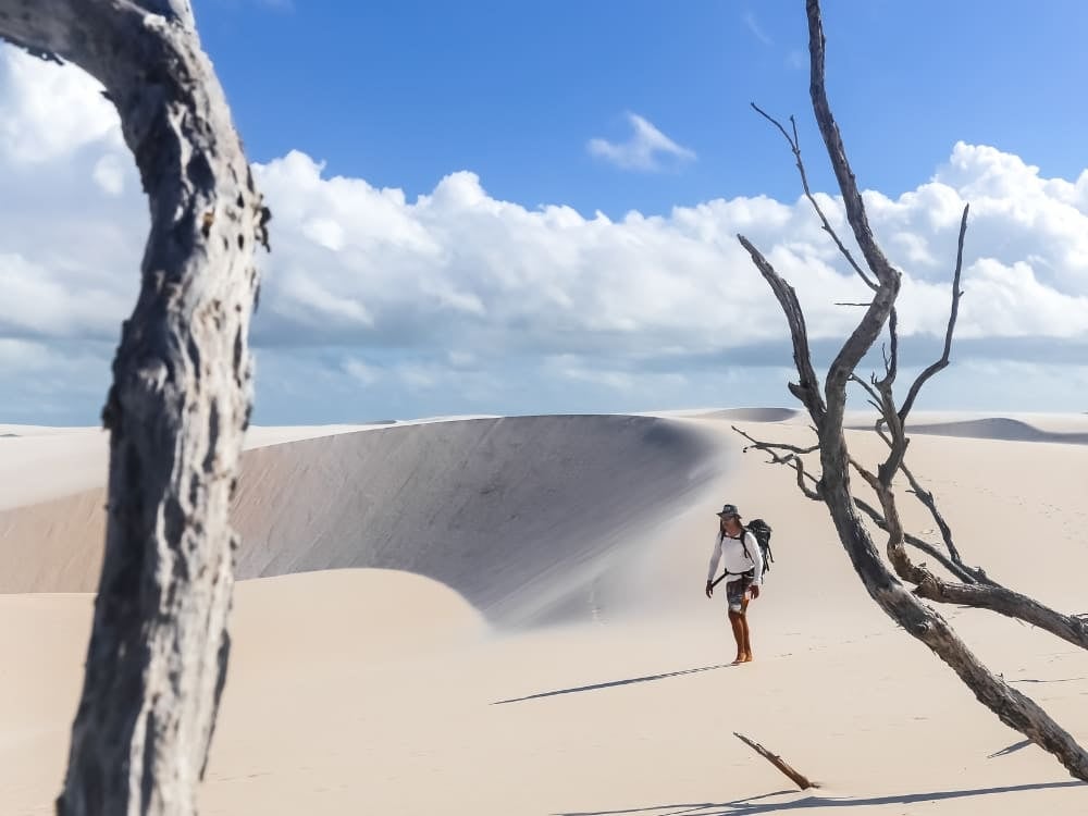 Um trilheiro explora as enormes dunas de areia branca do Parque Nacional dos Lençóis Maranhenses, emolduradas por galhos secos de árvores. Um trilheiro explora as enormes dunas de areia branca do Parque Nacional dos Lençóis Maranhenses, emolduradas por galhos secos de árvores.