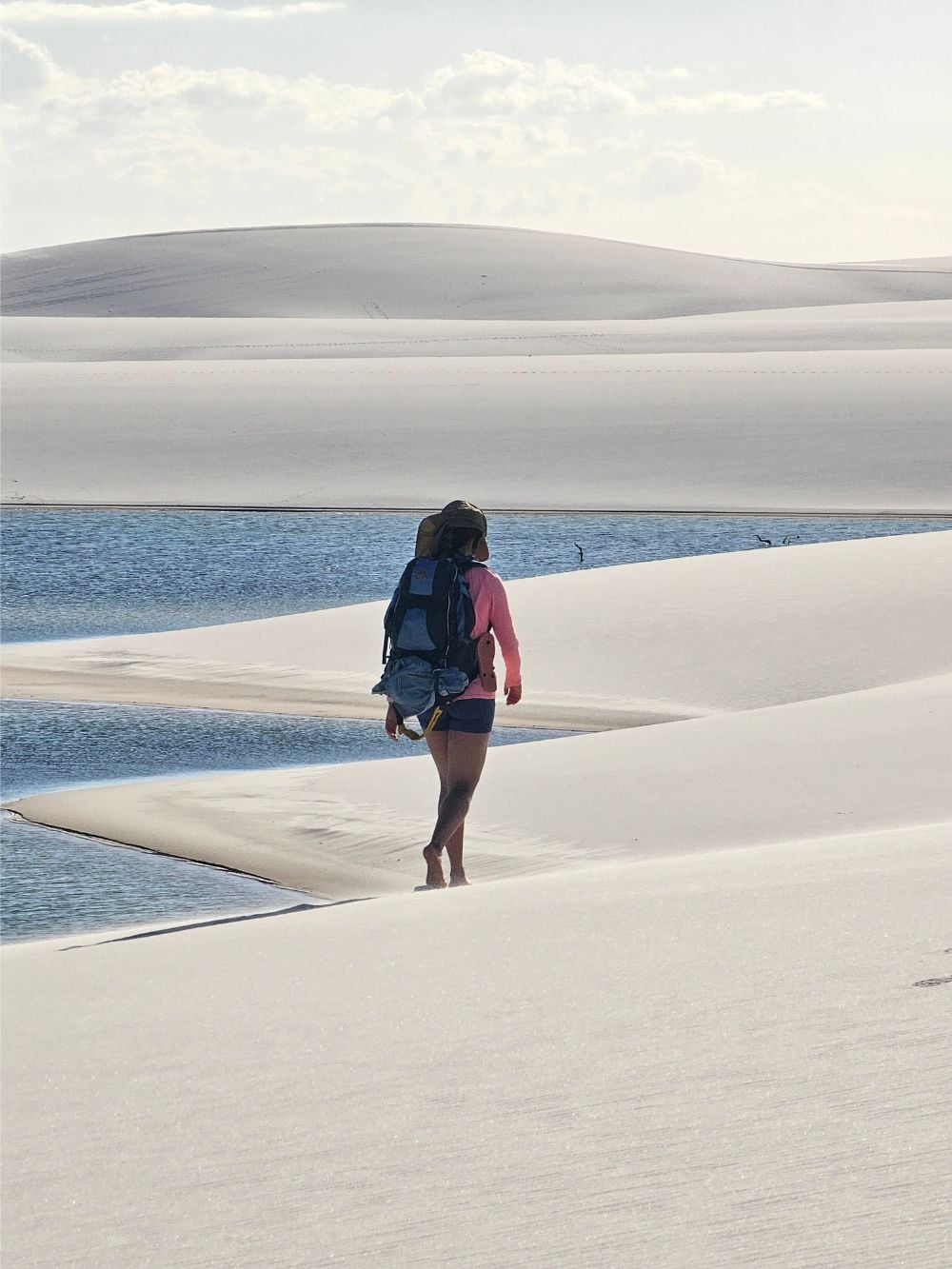 Um mochileiro caminha descalço pelas dunas de areia branca perto de uma lagoa azul de água da chuva durante um trekking no Parque Nacional dos Lençóis Maranhenses. Um mochileiro caminha descalço pelas dunas de areia branca perto de uma lagoa azul de água da chuva durante um trekking no Parque Nacional dos Lençóis Maranhenses.
