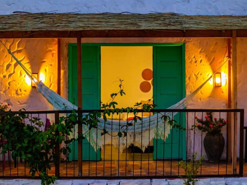 Intiem, 's nachts verlicht balkon met een hangmat gespannen voor de groene dubbele deur van een Quintal das Areias-chalet. Intiem, 's nachts verlicht balkon met een hangmat gespannen voor de groene dubbele deur van een Quintal das Areias-chalet.