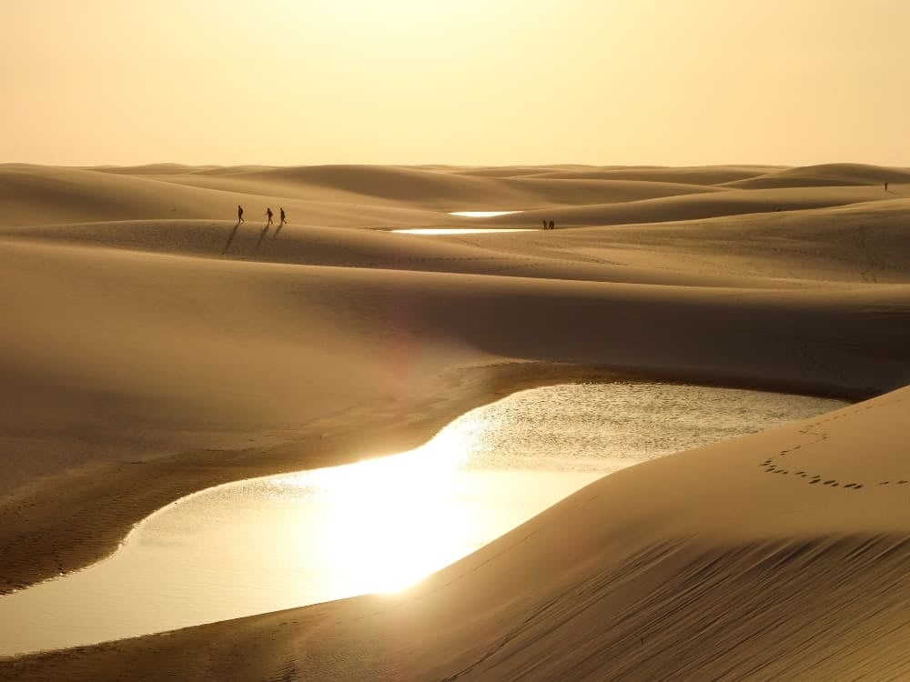 Viajantes caminham pela vasta extensão de dunas de areia nos Lençóis Maranhenses durante um pôr do sol brilhante. Viajantes caminham pela vasta extensão de dunas de areia nos Lençóis Maranhenses durante um pôr do sol brilhante.