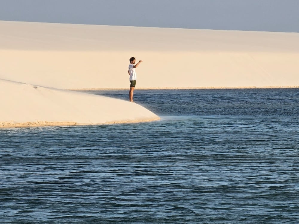Viajante em pé na beira de uma duna de areia clara apontando para as águas azuis profundas de uma lagoa nos Lençóis Maranhenses. Viajante em pé na beira de uma duna de areia clara apontando para as águas azuis profundas de uma lagoa nos Lençóis Maranhenses.