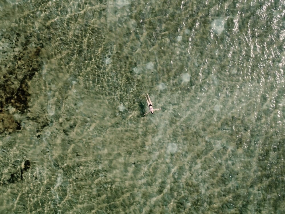 Vista de cima de uma pessoa nadando em uma lagoa cristalina de água da chuva nos Lençóis Maranhenses, revelando o fundo de areia. Vista de cima de uma pessoa nadando em uma lagoa cristalina de água da chuva nos Lençóis Maranhenses, revelando o fundo de areia.