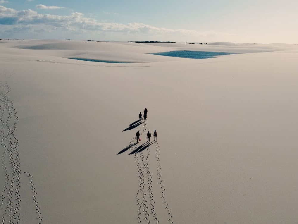 Um pequeno grupo de trilheiros projetando longas sombras enquanto caminha por uma vasta extensão de dunas de areia branca em uma travessia de vários dias nos Lençóis Maranhenses. Um pequeno grupo de trilheiros projetando longas sombras enquanto caminha por uma vasta extensão de dunas de areia branca em uma travessia de vários dias nos Lençóis Maranhenses.