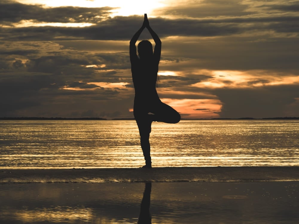Silhouette of a person doing a yoga tree pose on an Amazon river beach at sunset. Silhouette einer Person, die bei Sonnenuntergang an einem Amazonas-Flussstrand die Yoga-Baum-Pose macht.